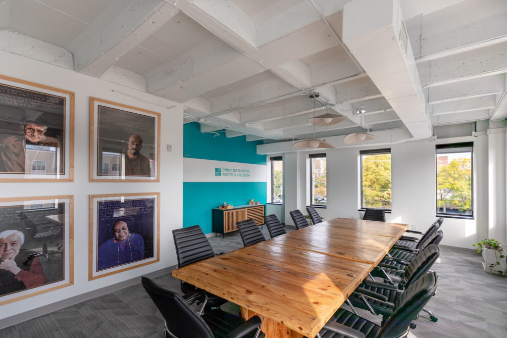A Commercial interior design done by TEW Design Studio featuring four pictures on the far left wall and a large rectangular wooden table in the middle of the room surrounded by twelve chairs in a office building in Apex. 