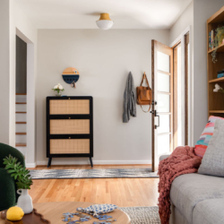 Open-concept living room and entryway featuring wall cut-outs, rattan shoe cabinet, grey sofa and plenty of colorful pops.