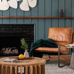 Modern Raleigh living room with warm leather seating, green paneling, sconces, a modern coffee table, black fireplace and sculptural artwork.
