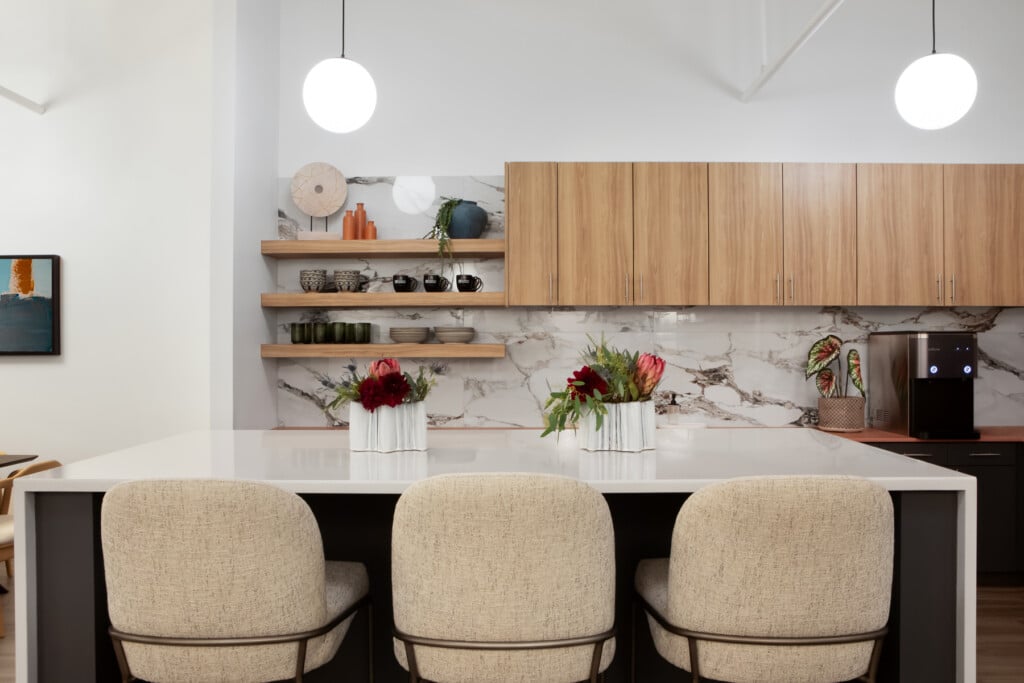 Three high-top chairs at a kitchenette island countertop in workplace breakroom designed for employee wellness - TEW Design Studio